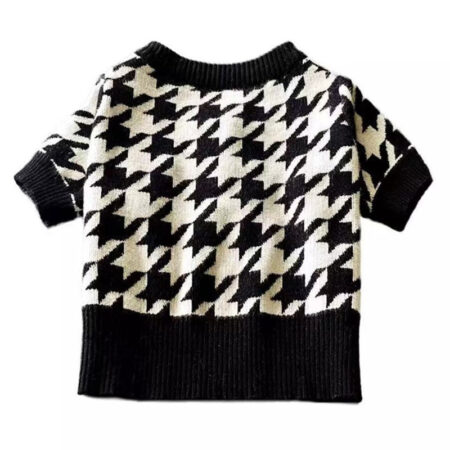 Black and white houndstooth knit dog sweater with ribbed collar and cuffs on wooden chair