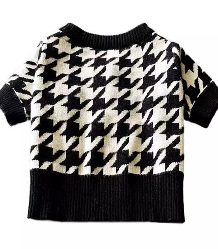 Black and white houndstooth knit dog sweater with ribbed collar and cuffs on wooden chair