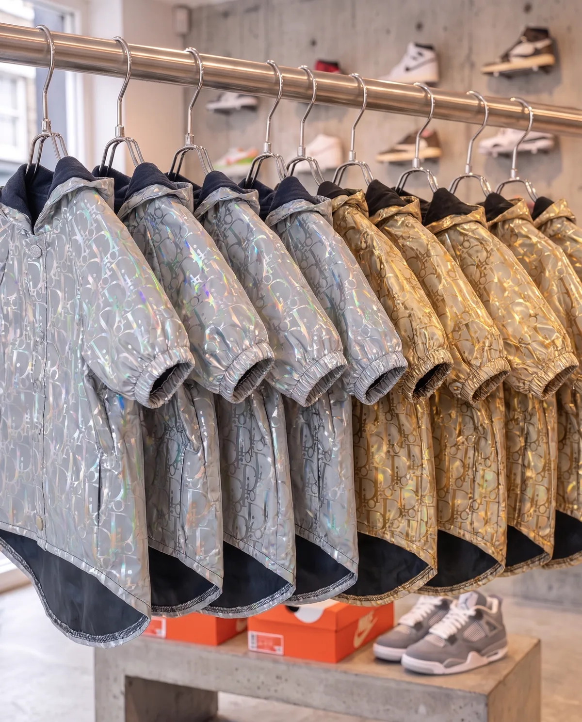 Dogior Reflective Windbreakers (in silver and gold) on a chrome rack in a sneaker shop, flash off