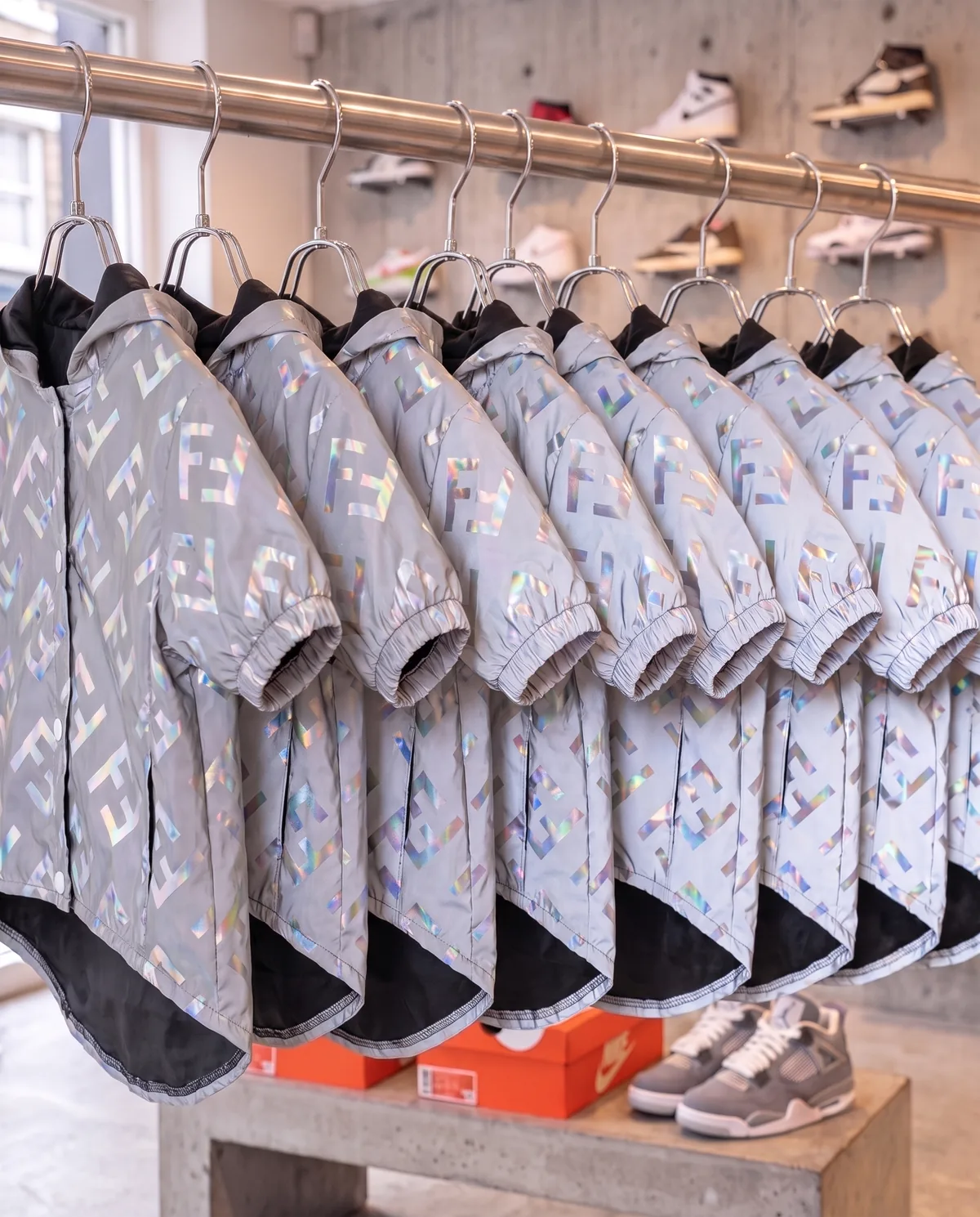 Furdi Reflective Windbreakers (holographic silver with FF monogram) on a chrome rack in a sneaker shop, flash off