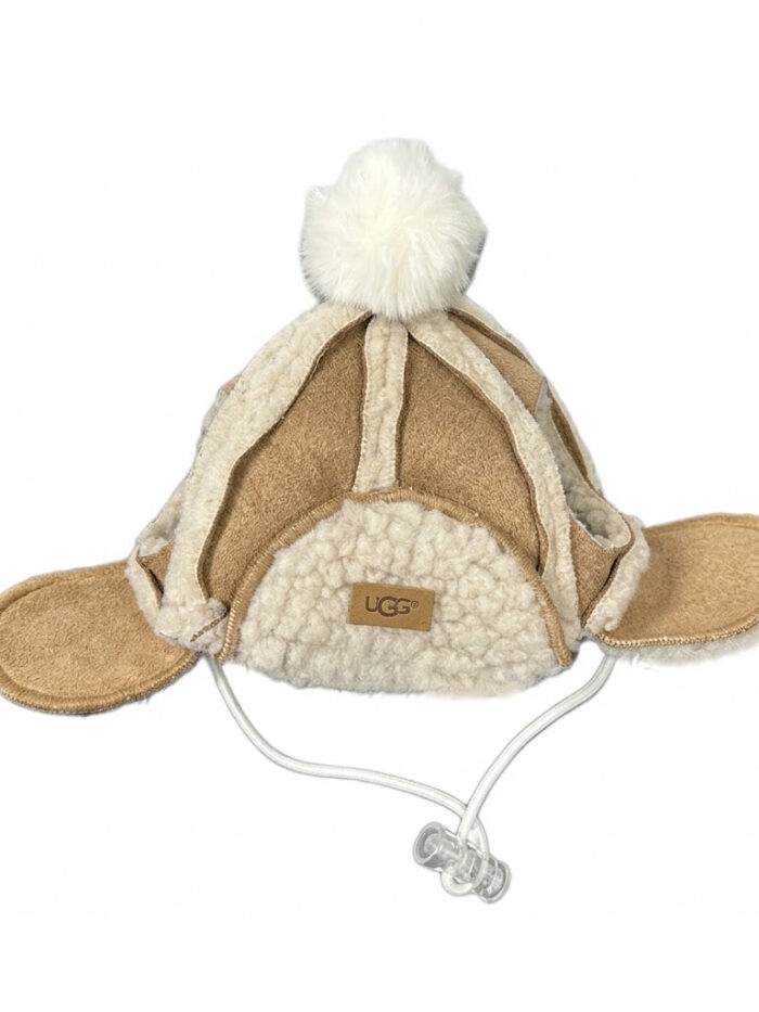 Brown sherpa-lined dog winter hat with white pom pom and ear flaps UGG style on white background